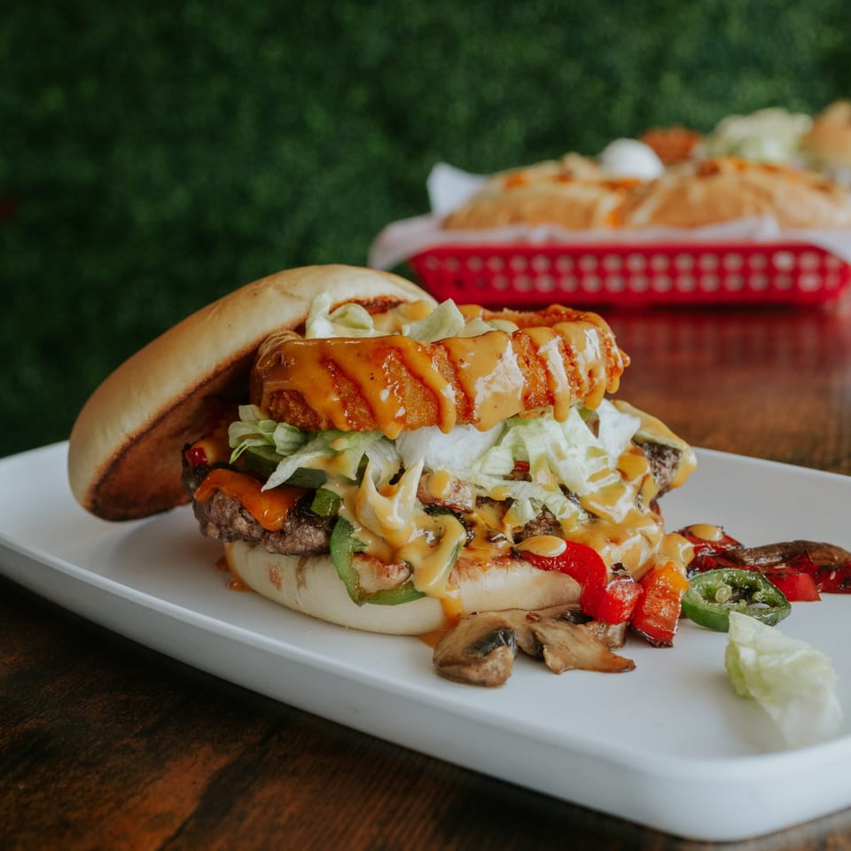 Close view of a stacked burger with grilled vegetables and sauce.