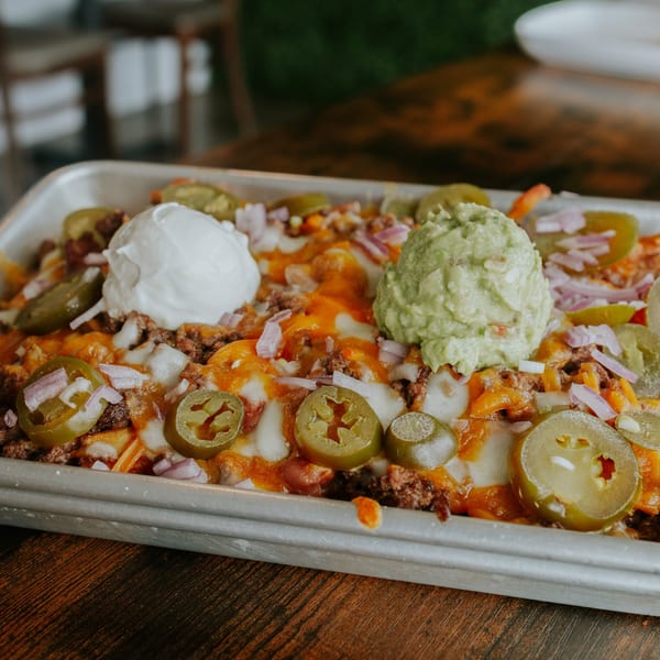 Close-up of loaded nachos with melted cheese, jalapeños, guacamole, and sour cream.