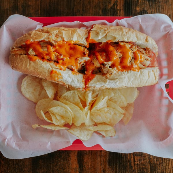 Overhead view of a saucy chicken sub served with potato chips.